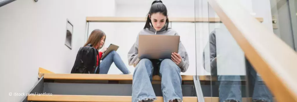 Ein Schülerin sitzt mit Laptop in einem Treppenhaus