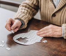 Ein älterer Mensch setzt ein Puzzles zusammen, das die Form eines Kopfes hat.