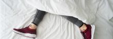 Frau liegt mit Sportschuhen im Bett